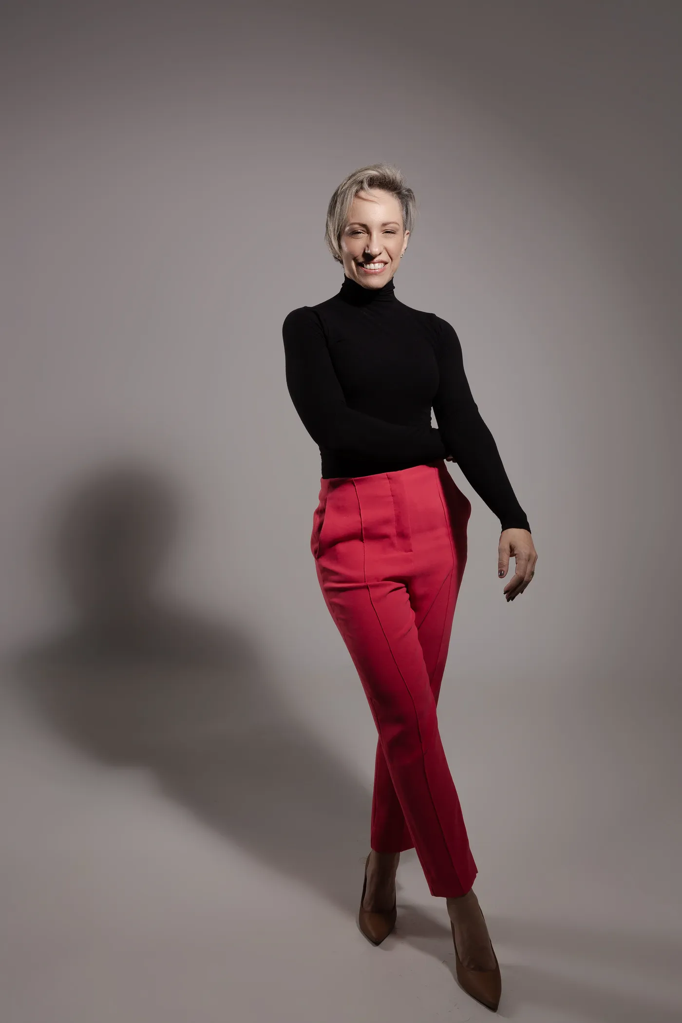 Luciana Dentello em pé, de blusa preta e calça vermelha